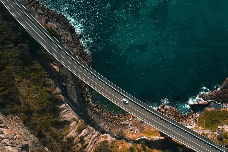 A vehicle driving over a bridge across a part of ocean