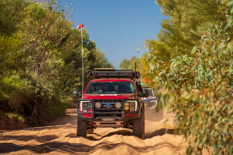 Ford 4x4 driving through sandy forest in convoy