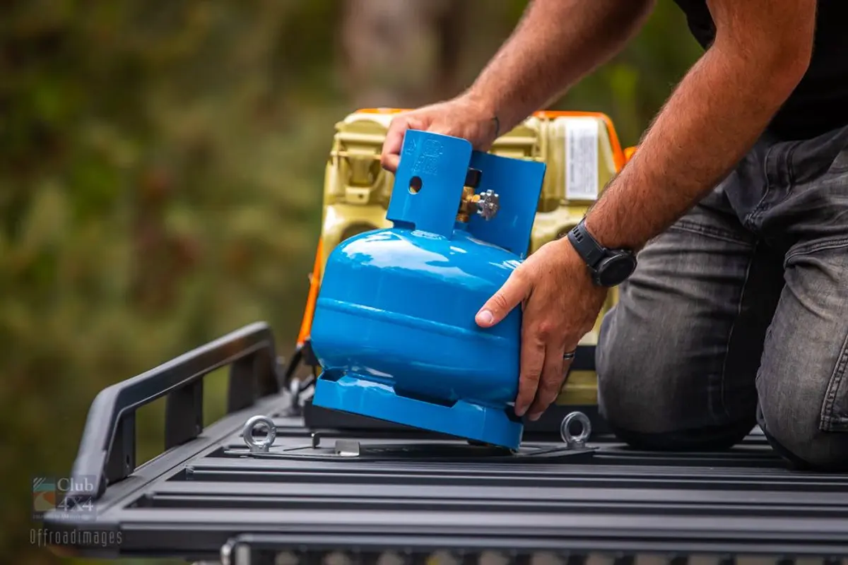 person tying down gas bottle on 4wd roof rack camping