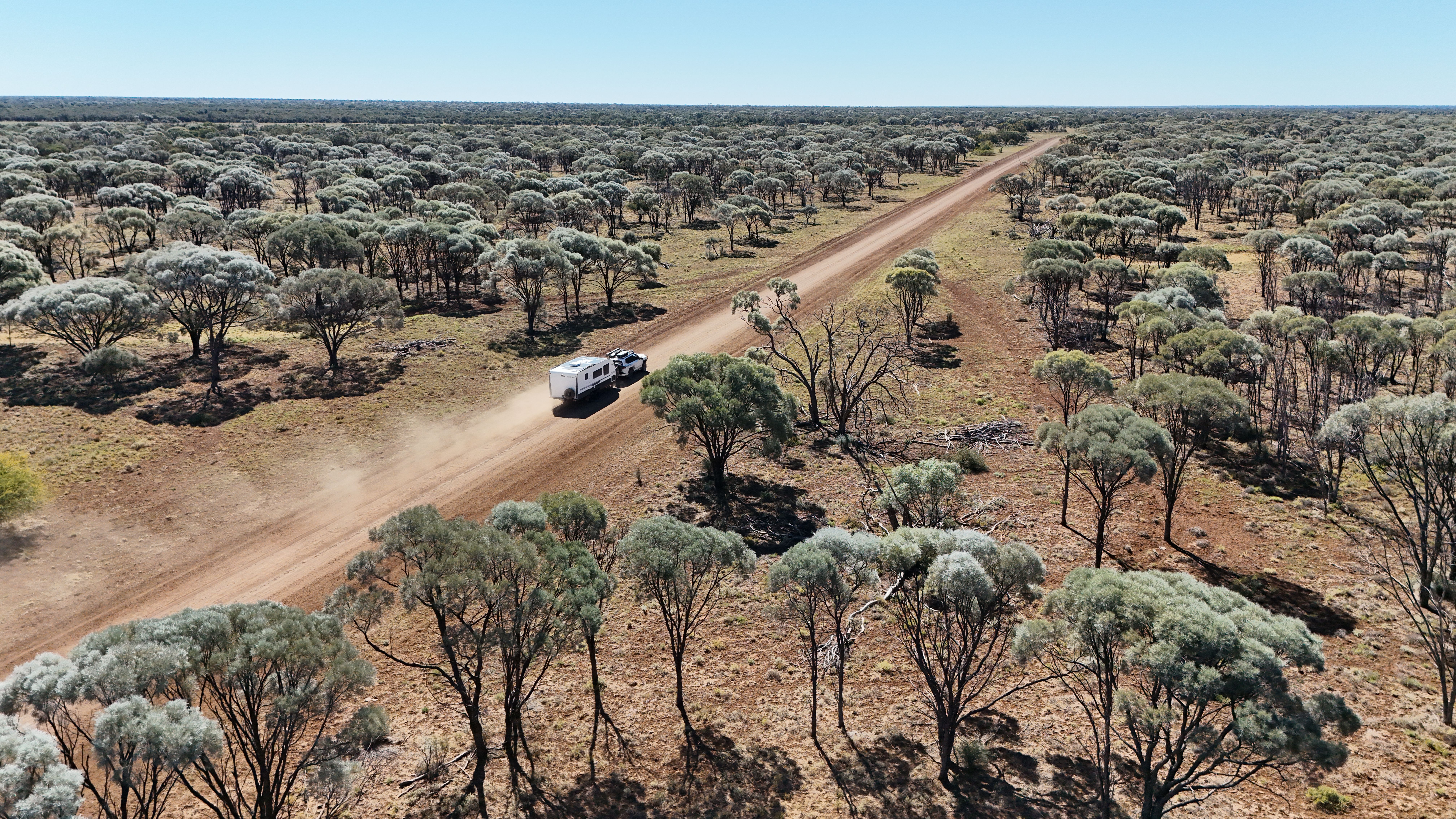 a vehicle driving through a dusty road with sparse trees