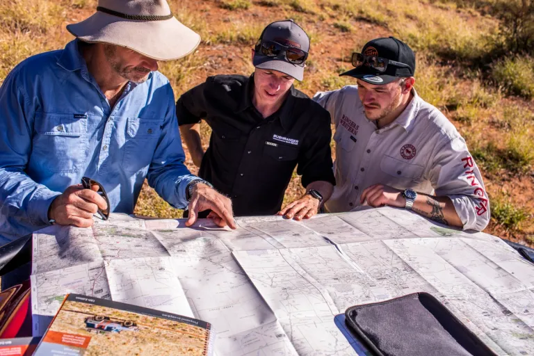 three men inspecting a map on the bonnet of a 4wd