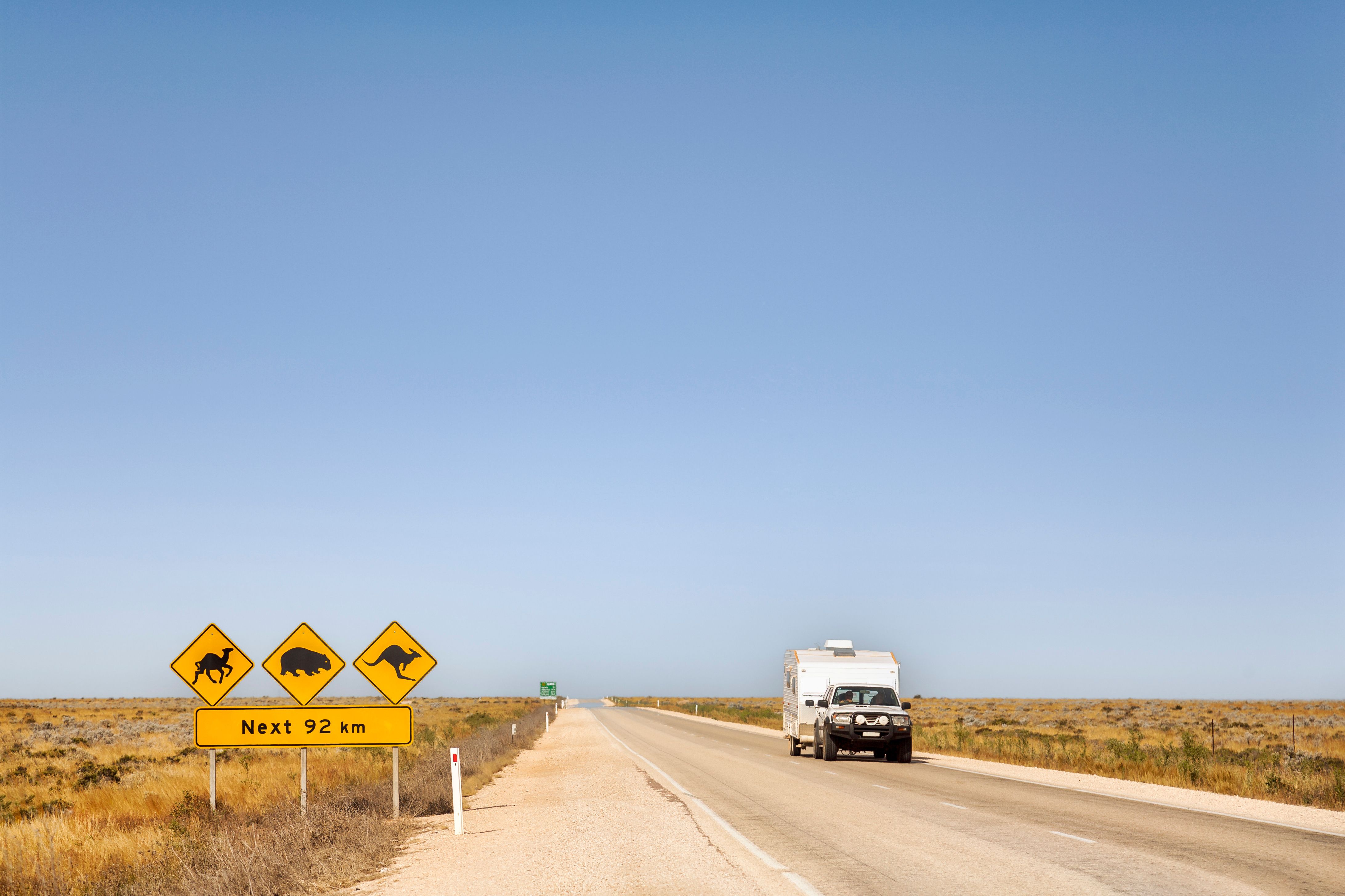 A vehicle towing a caravan along an Australian highway with road signs of animals