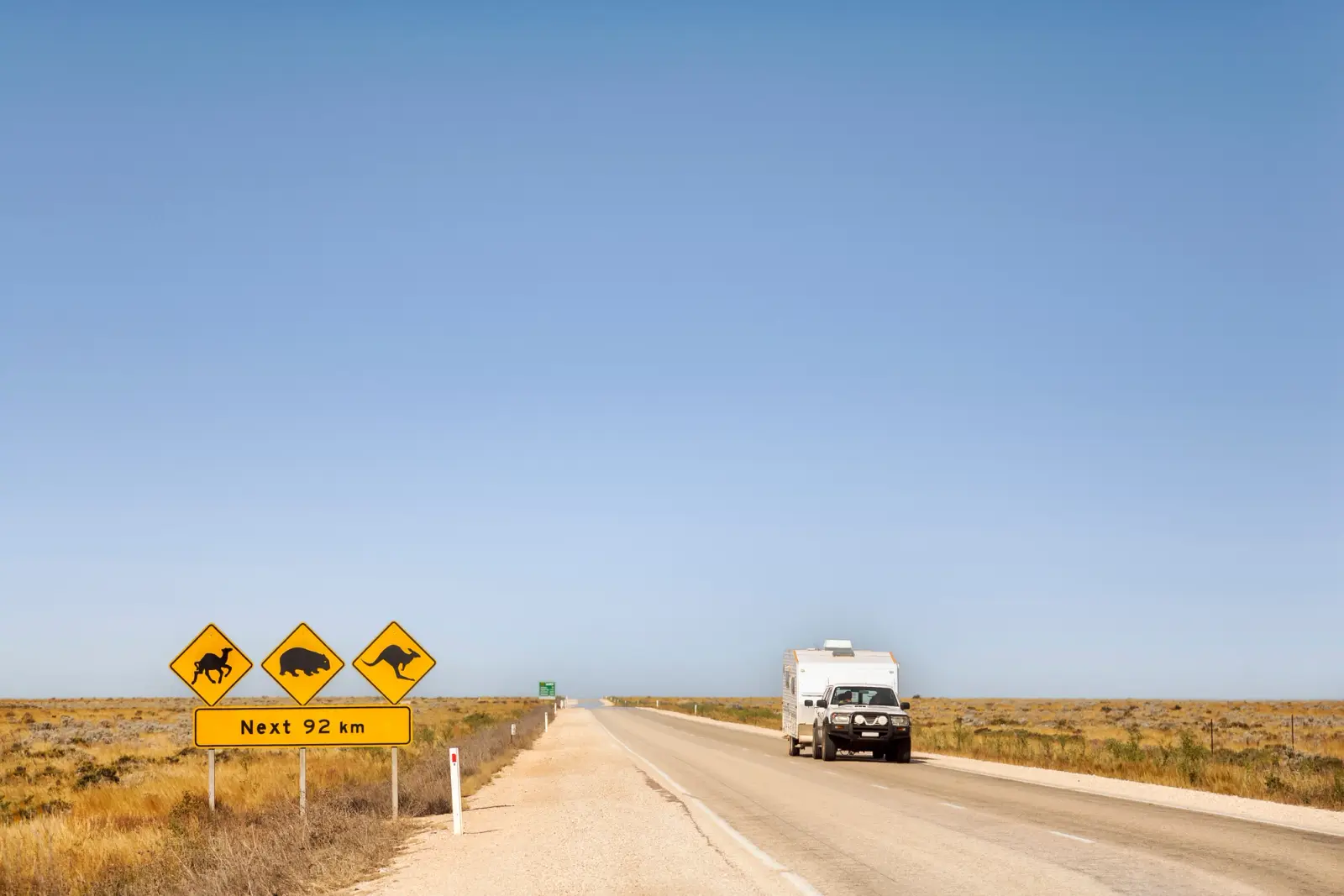 A vehicle towing a caravan along an Australian highway with road signs of animals