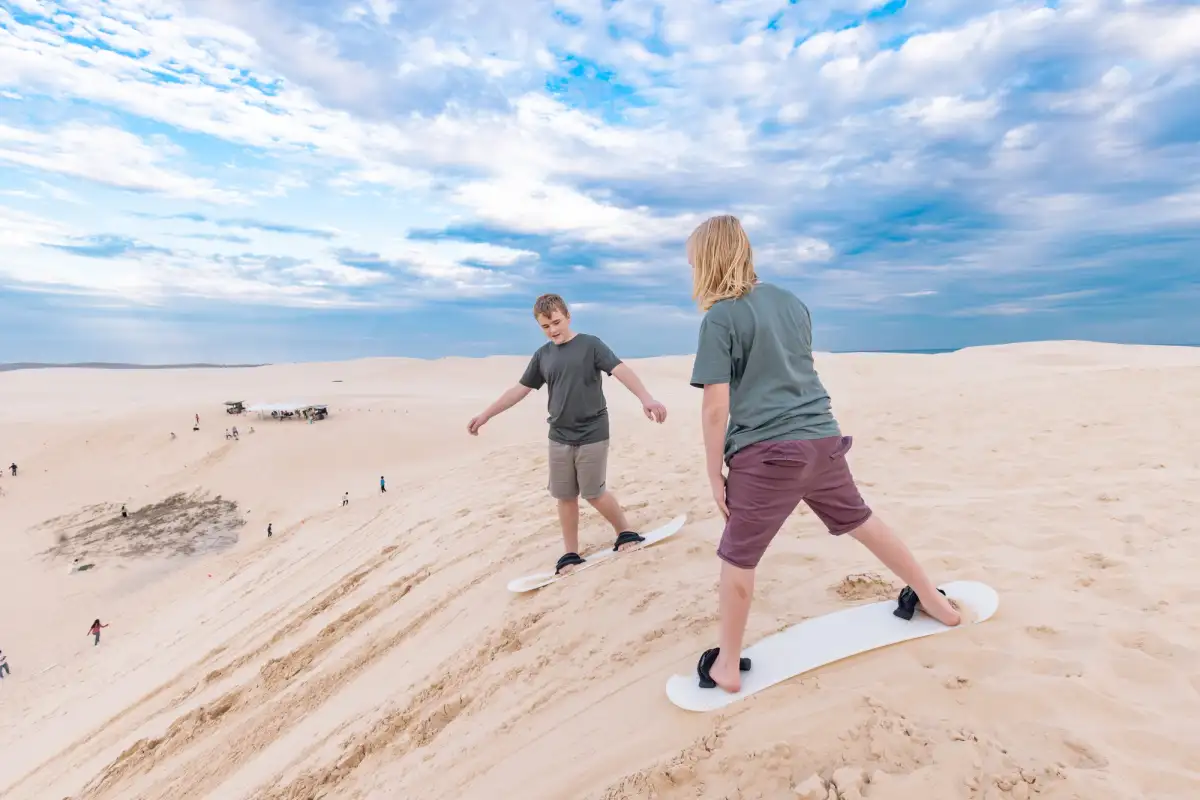 2 kids sandboarding at Stockton Beach