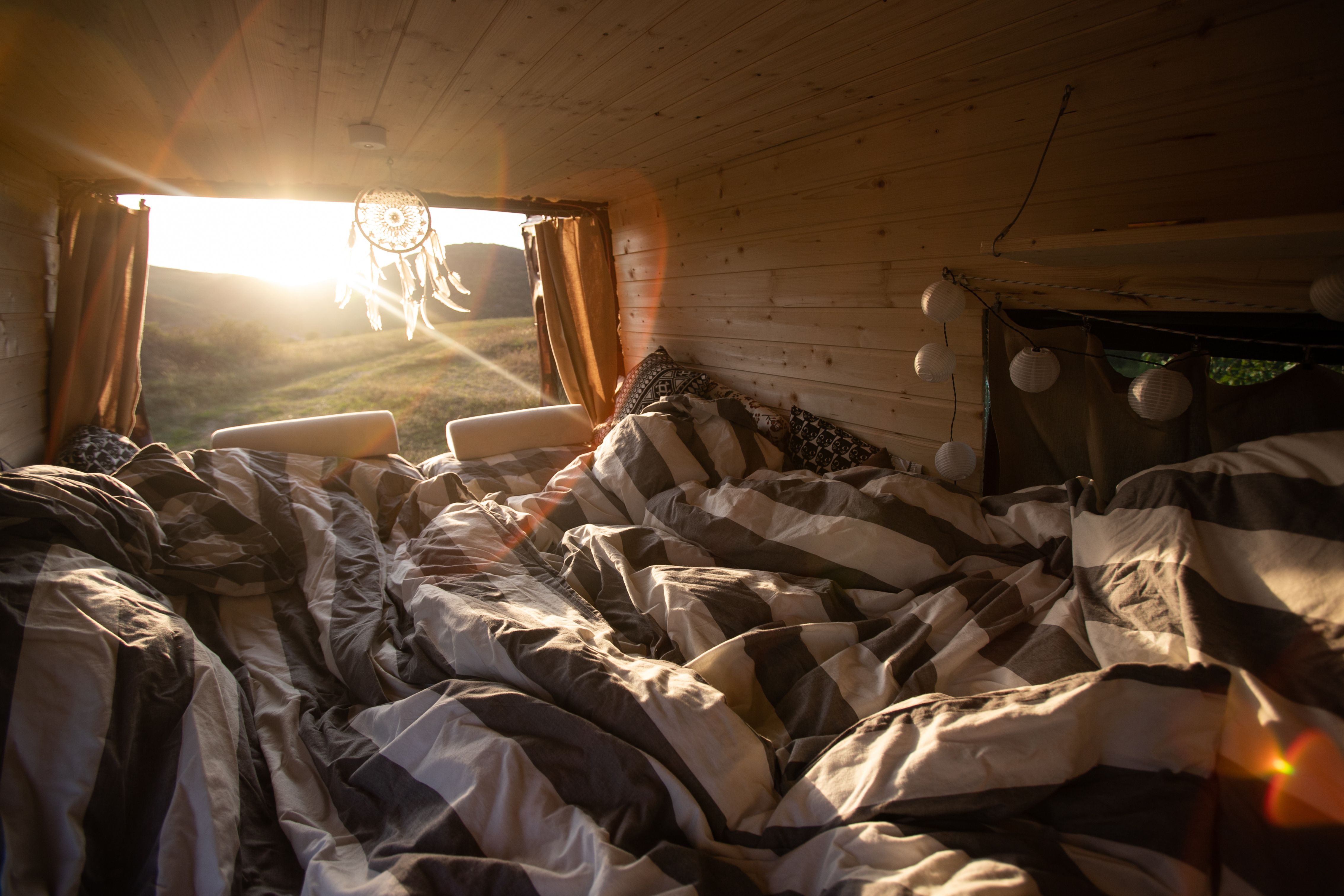A campervan with plywood walls and ceiling with an open back door and bed