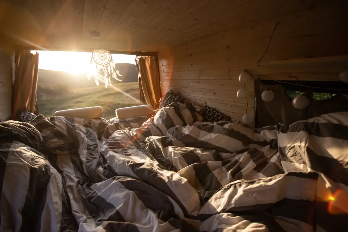A campervan with plywood walls and ceiling with an open back door and bed