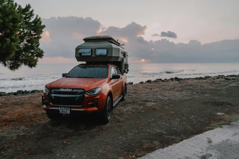 orange 4x4 with camper on back in front of beach and sunset
