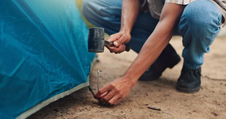 person using a mallet to hammer a tent peg into the ground