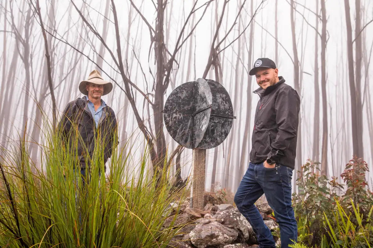 two men in a forest posing with a sign