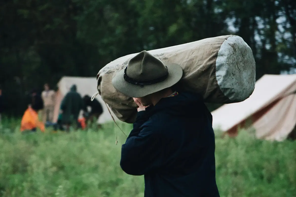 man carrying a swag at a campsite