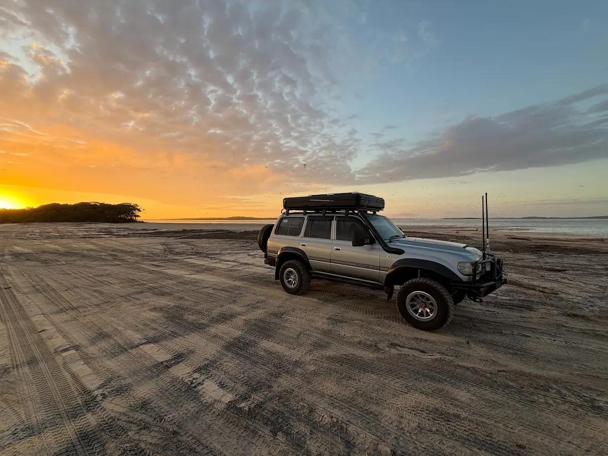 An 80 Series LandCruiser on a beach with a sunset