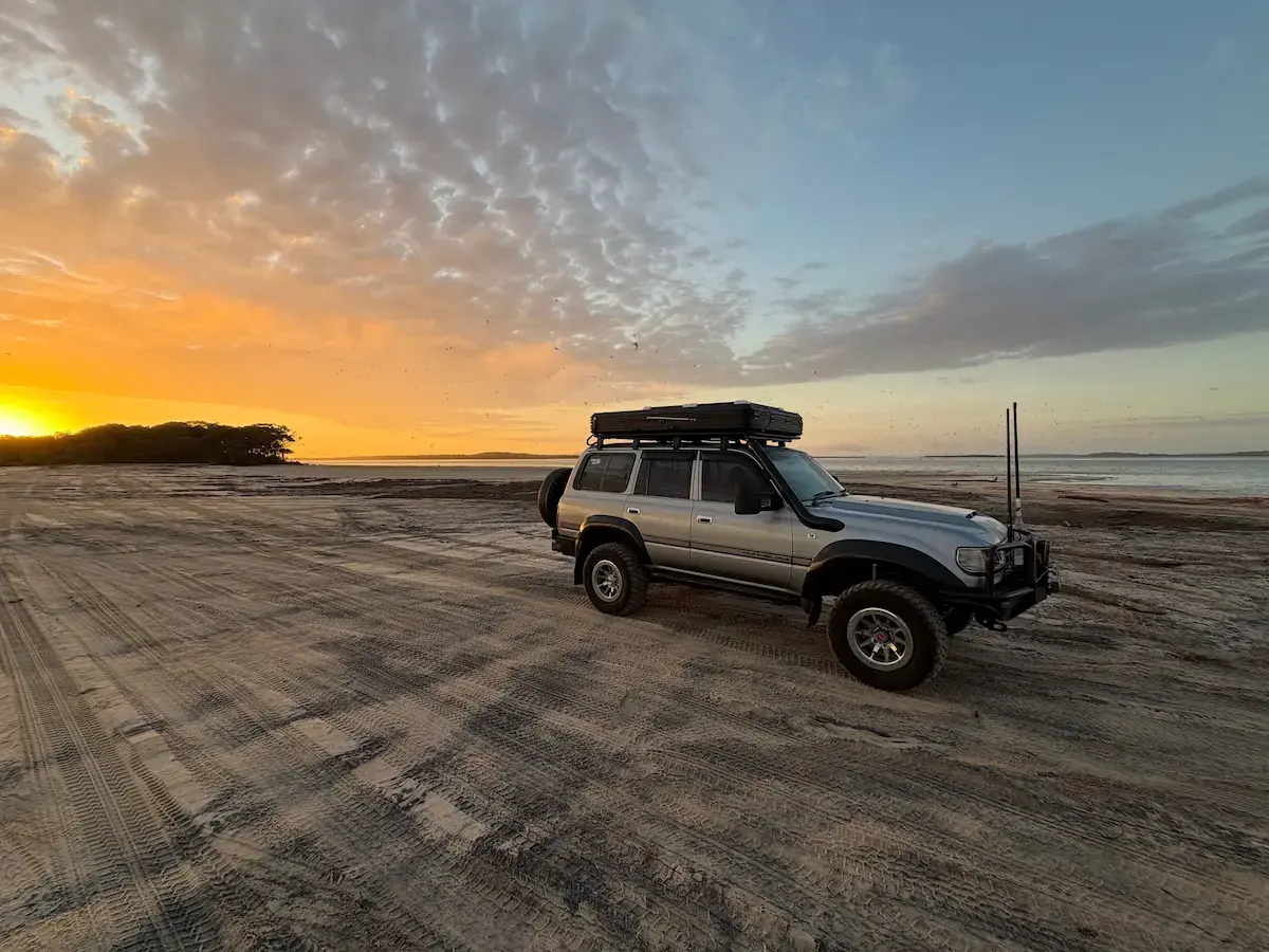 An 80 Series LandCruiser on a beach with a sunset