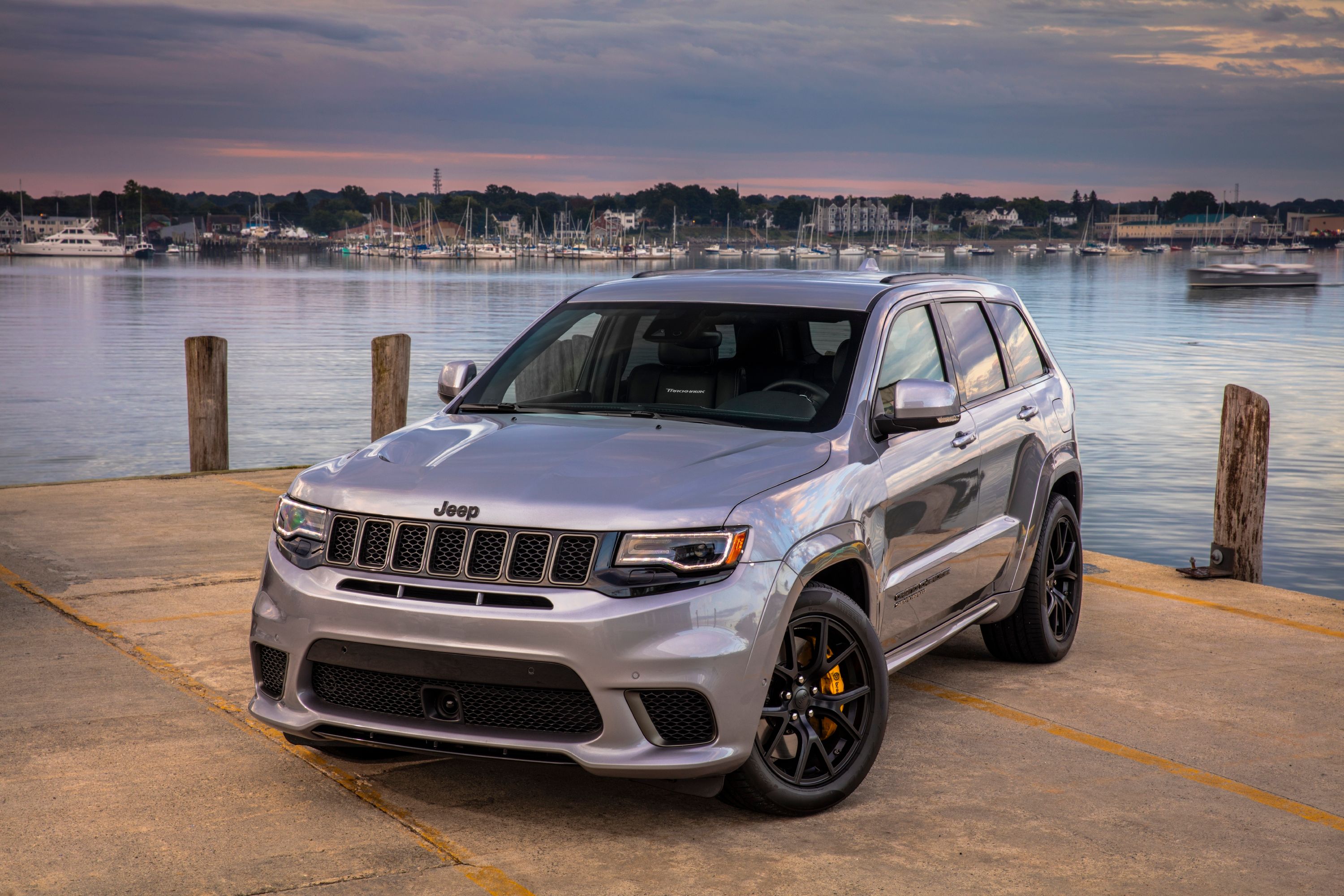 A silver grey Jeep Grand Cherokee Trackhawk near the water at sunset