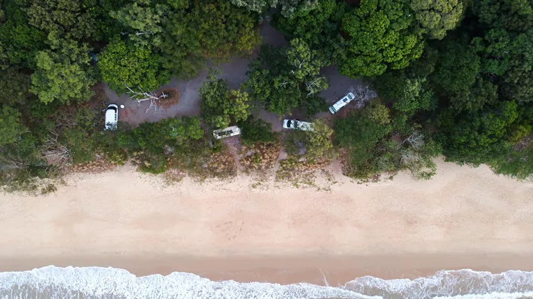 camper vans in a camp site on a tropical beach with trees