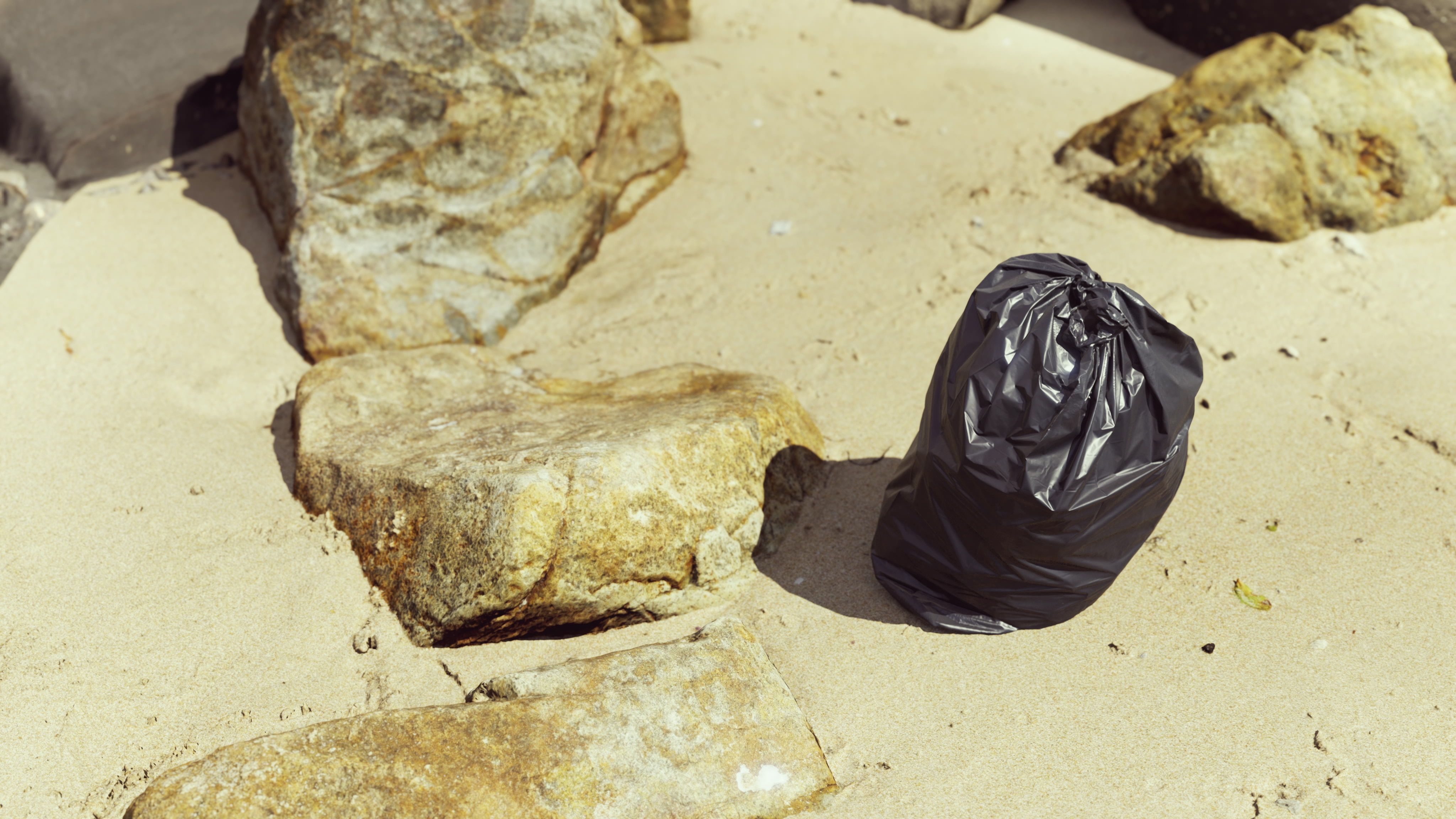 a bin bag on sand next to rocks