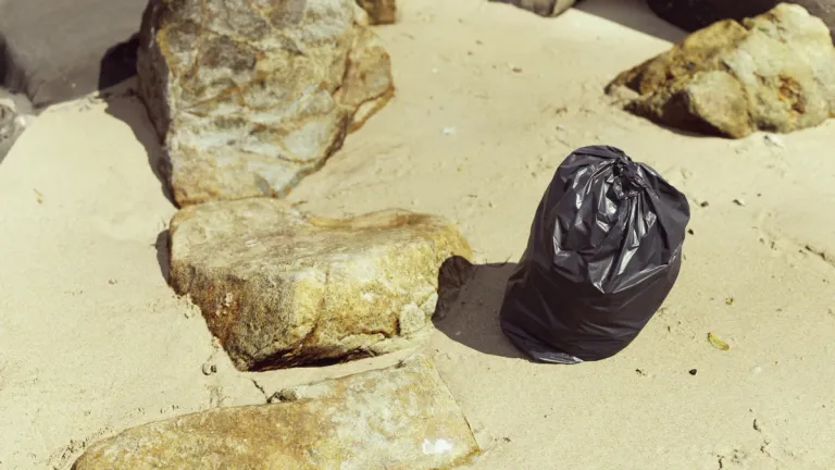a bin bag on sand next to rocks