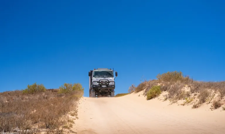 A 4X4 truck driving over a sand dune hill