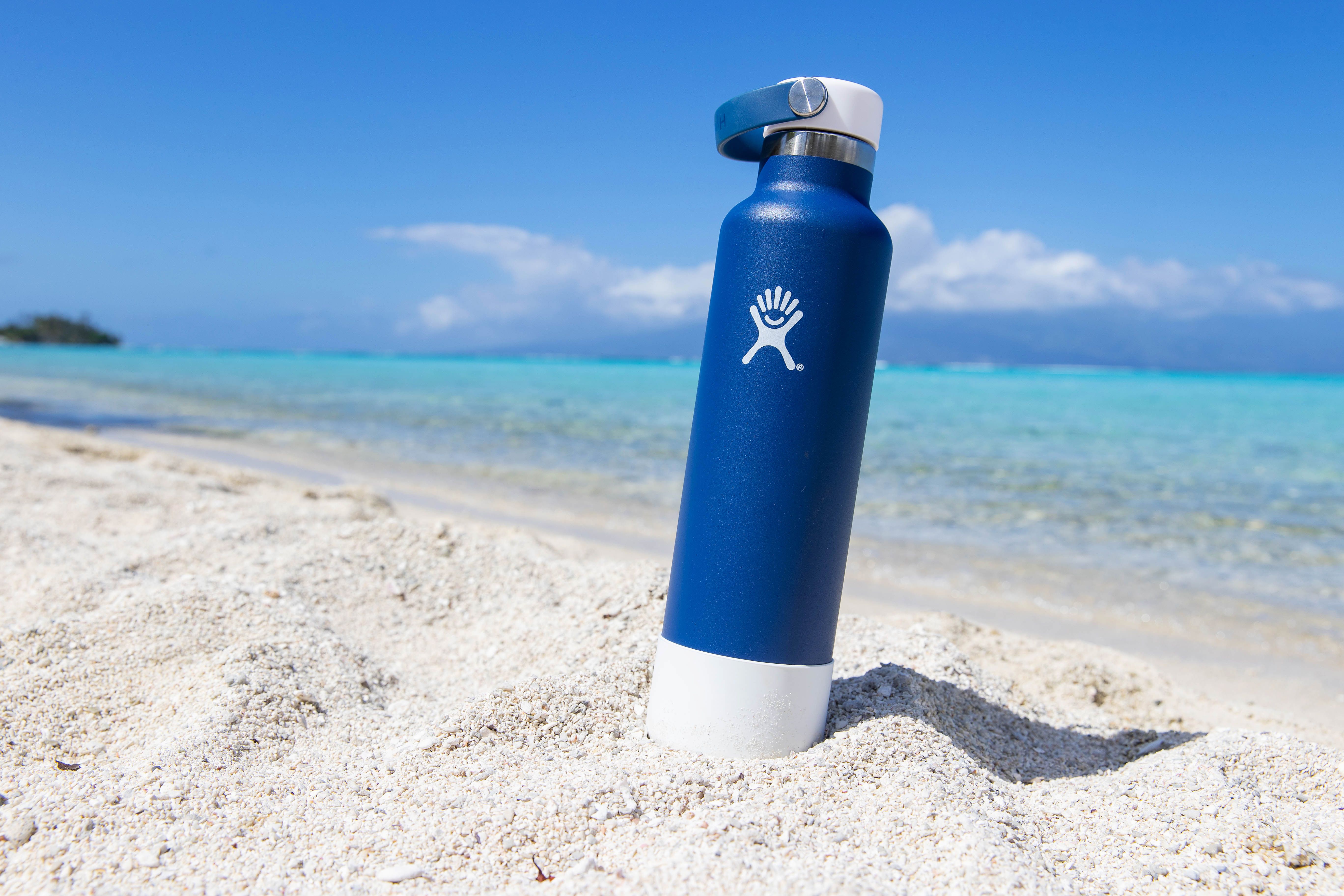 General view of blue hydro flask water bottle on sandy ocean beach at tropical island 