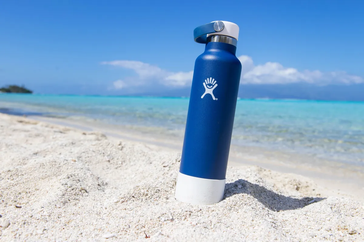 General view of blue hydro flask water bottle on sandy ocean beach at tropical island