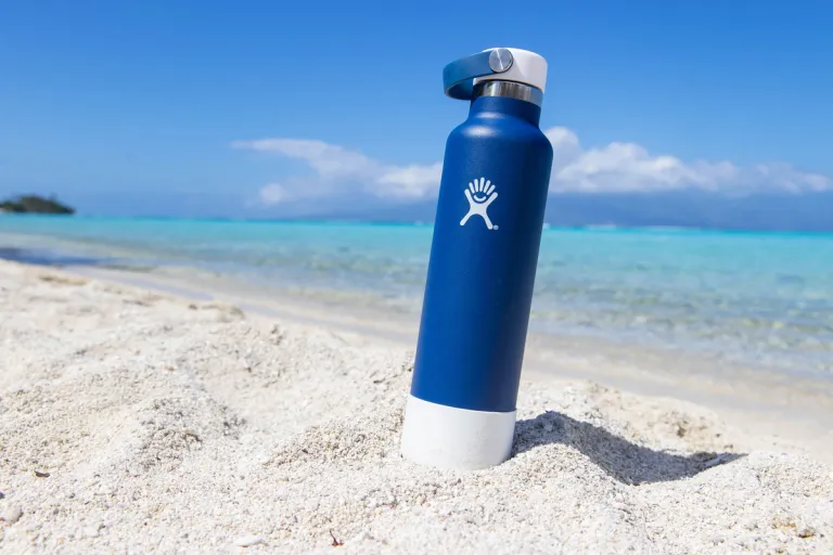 General view of blue hydro flask water bottle on sandy ocean beach at tropical island