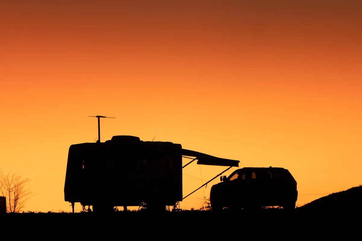 The silhouette of a car and caravan in front of a sunset
