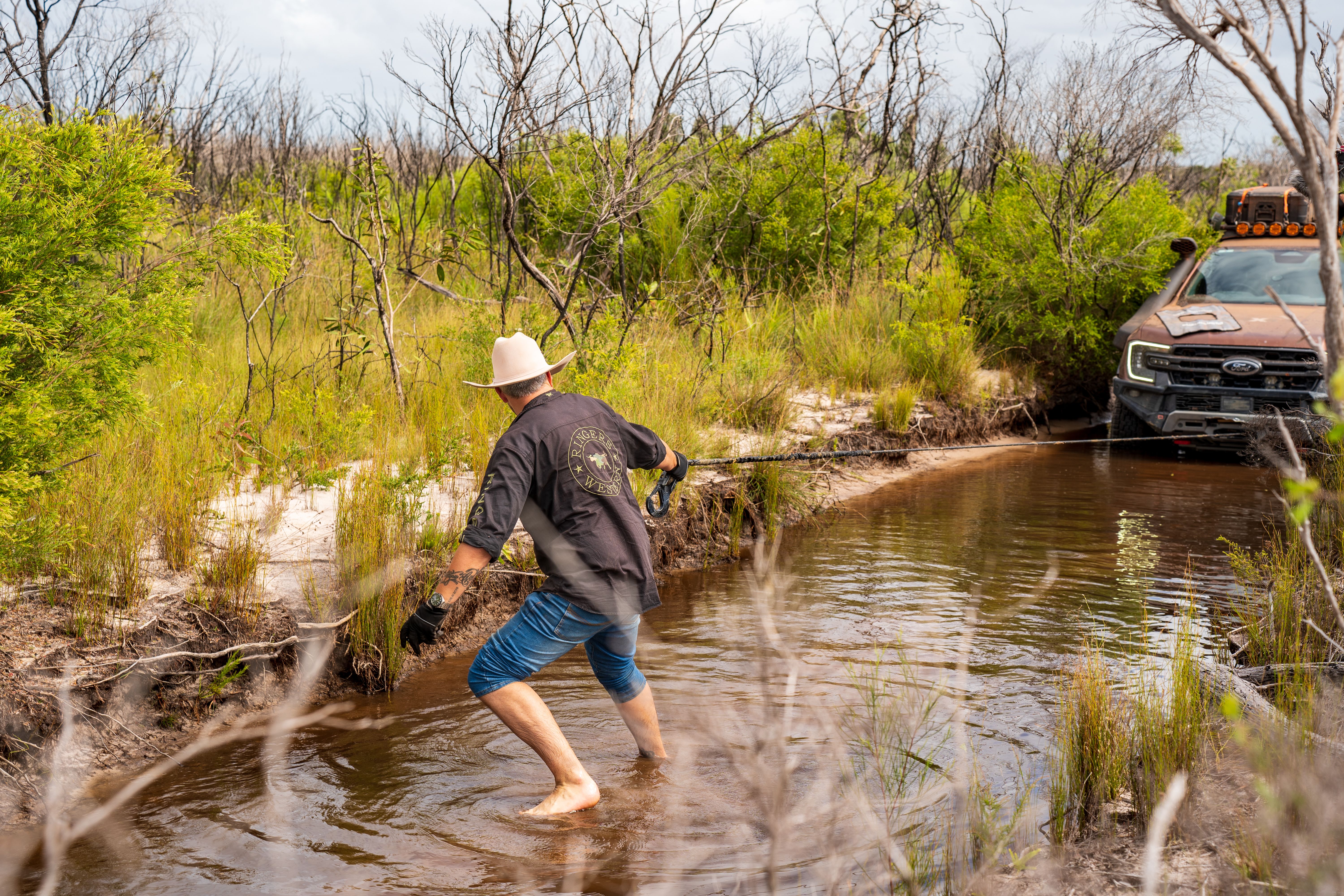 man extending a winch wire from a bogged 4wd through a muddy area