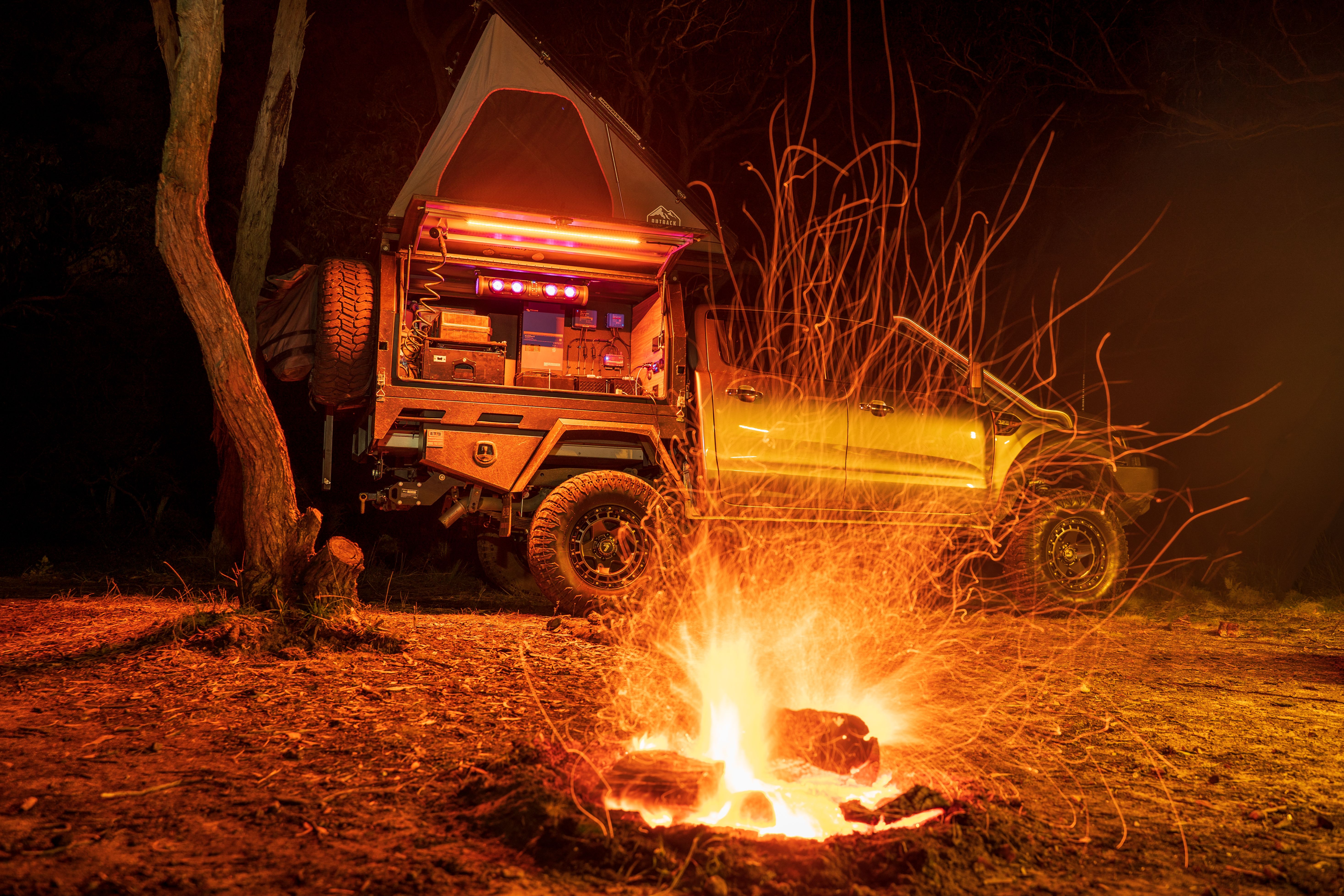 A 4X4 Ford Range with a popped rooftop tent behind a campfire in the bush at night