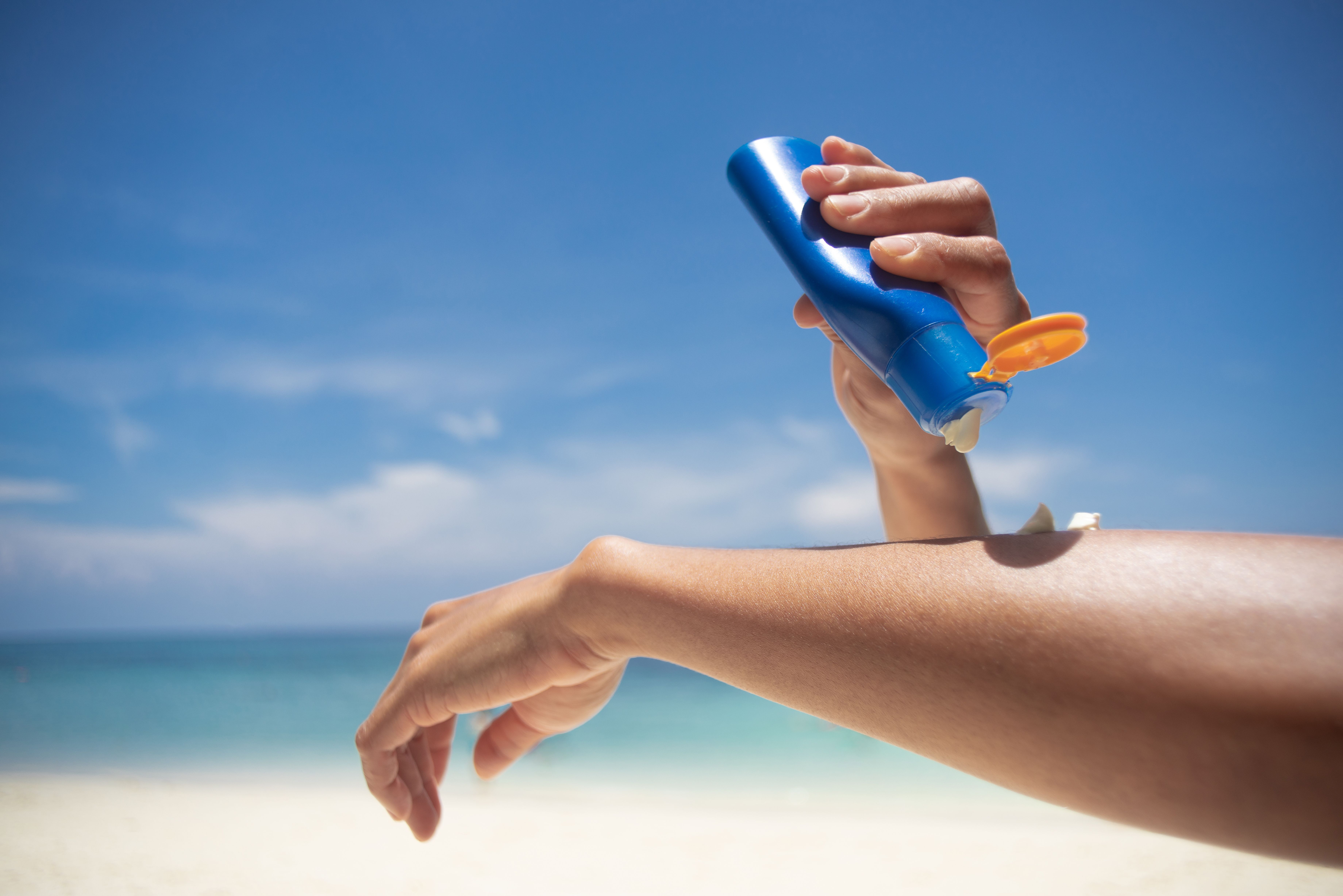 A person applying sunscreen to their arm on the beach