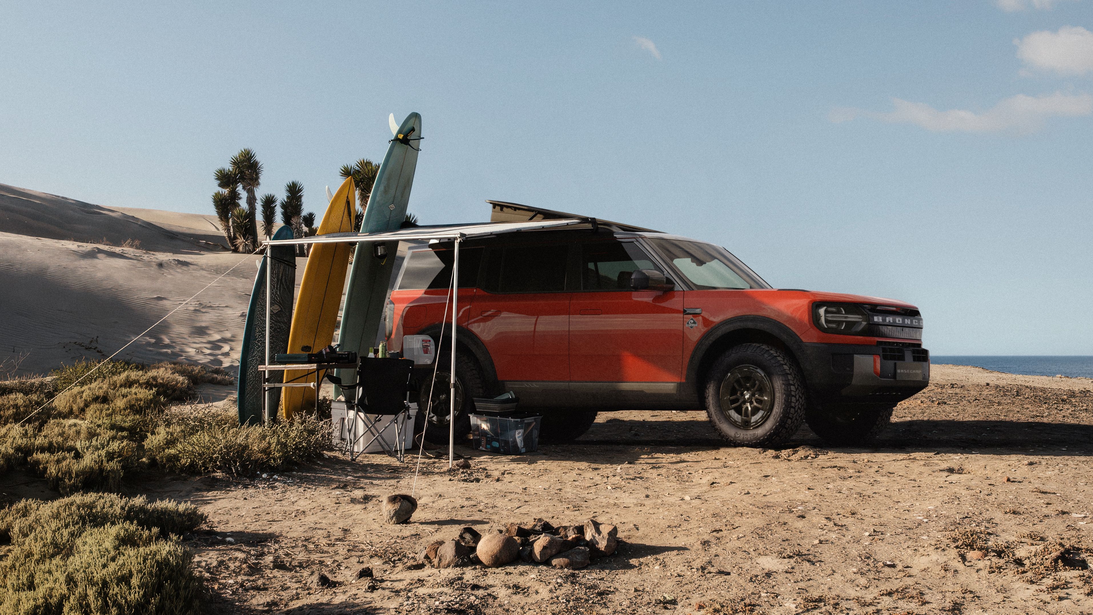 2027 Ford Bronco Basecamp on the beach by a rack of surfboards