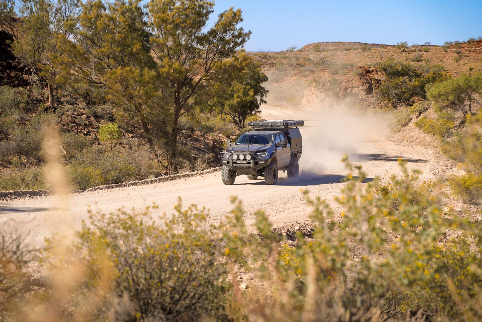 4wd driving through an outback track kicking up red dust