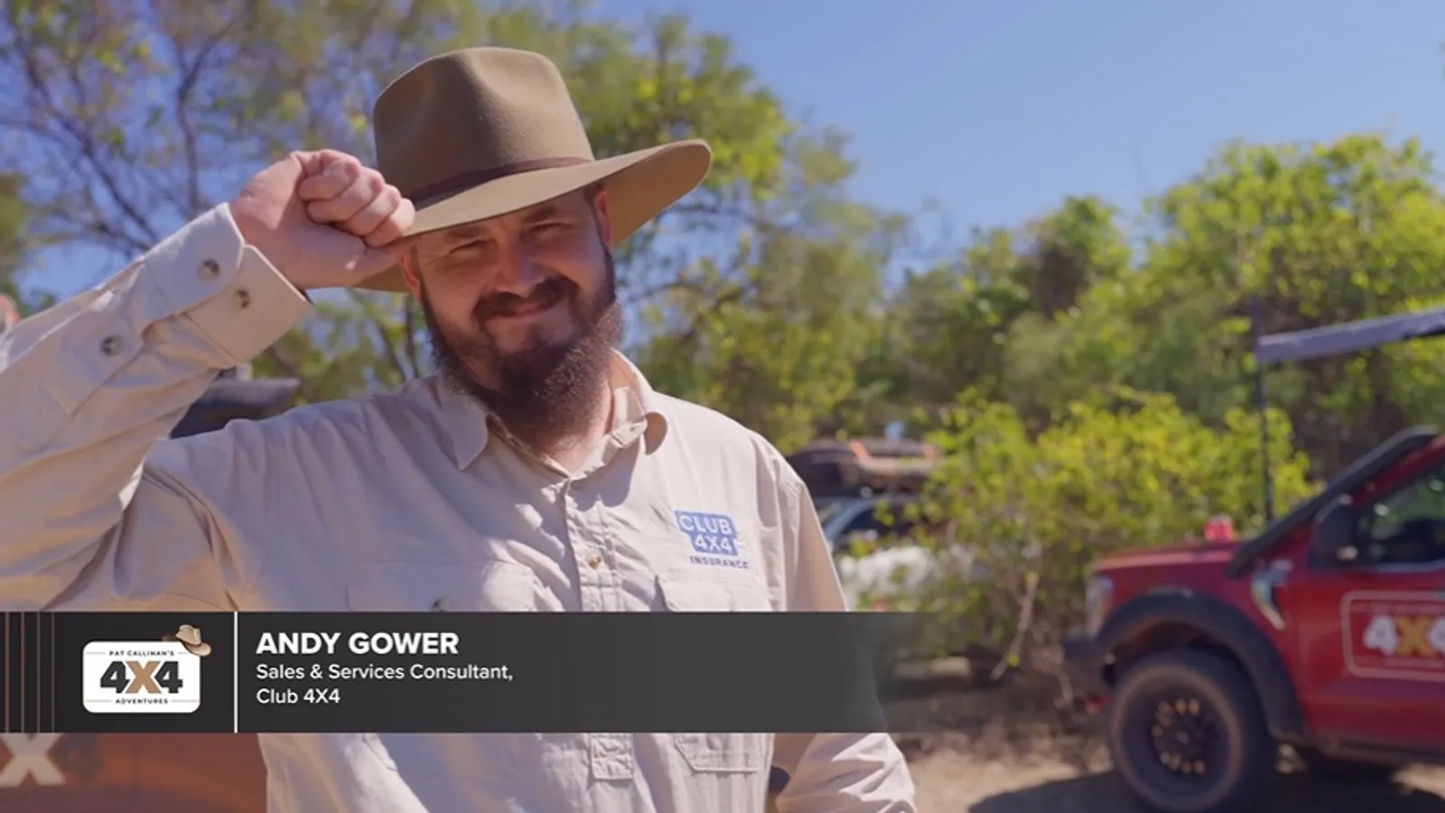 man tipping his hat while smiling in front of a red 4X4