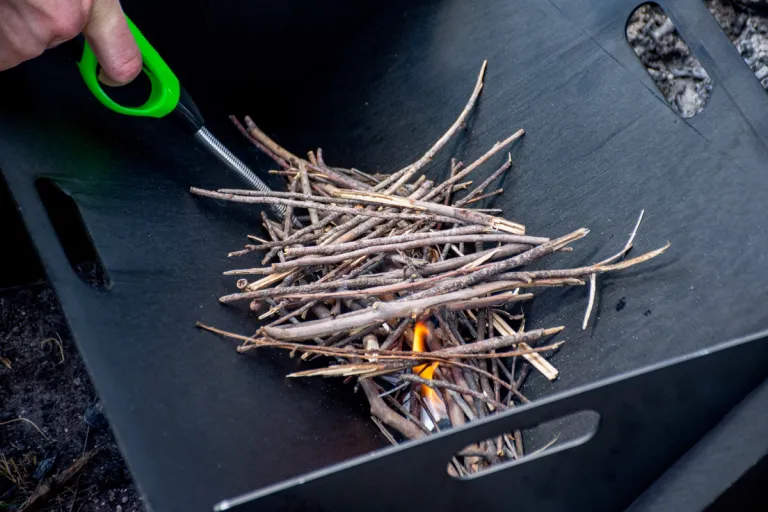 a long-necked lighter lighting some kindling in a campfire