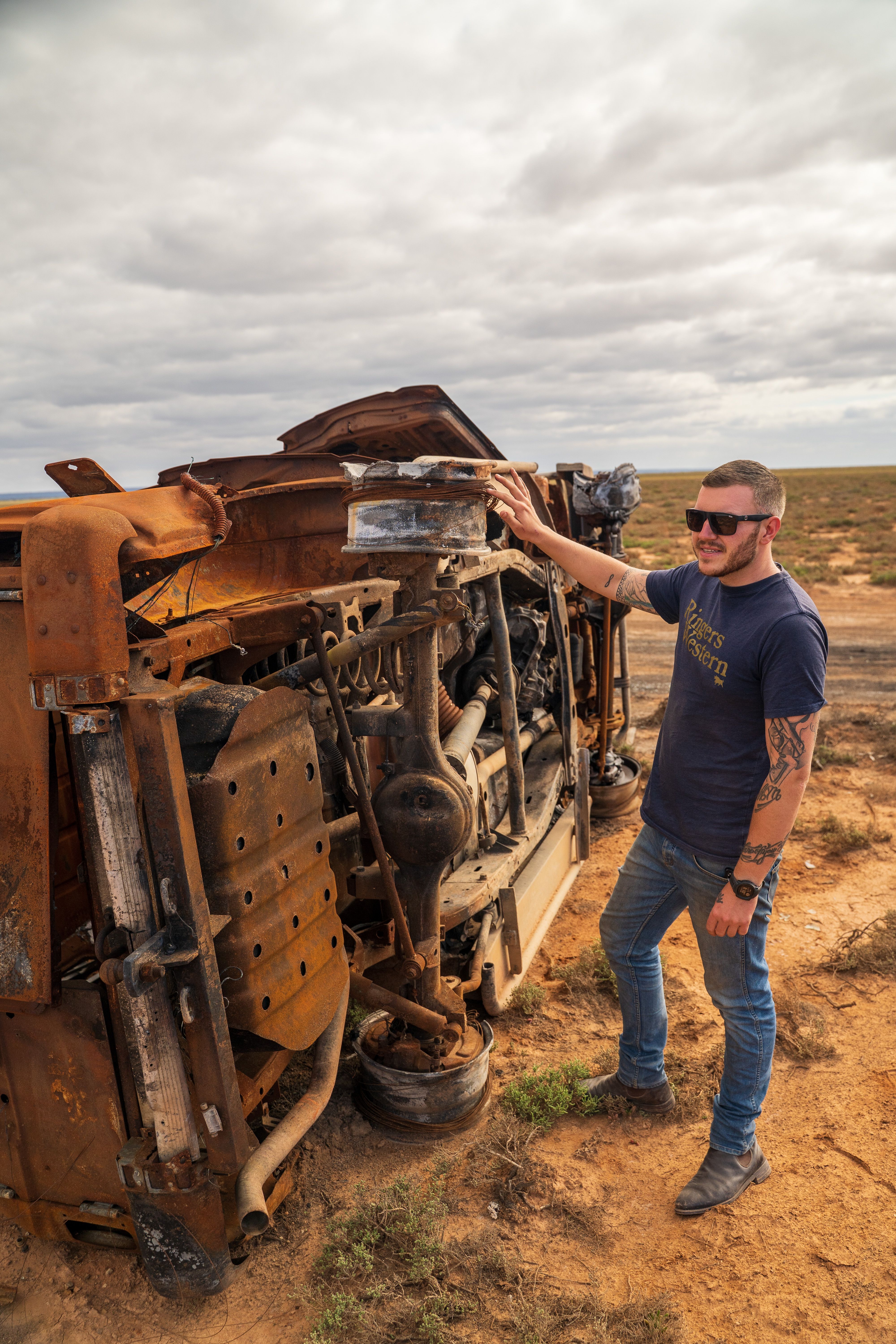 A man standing by a rusted car in the Outback