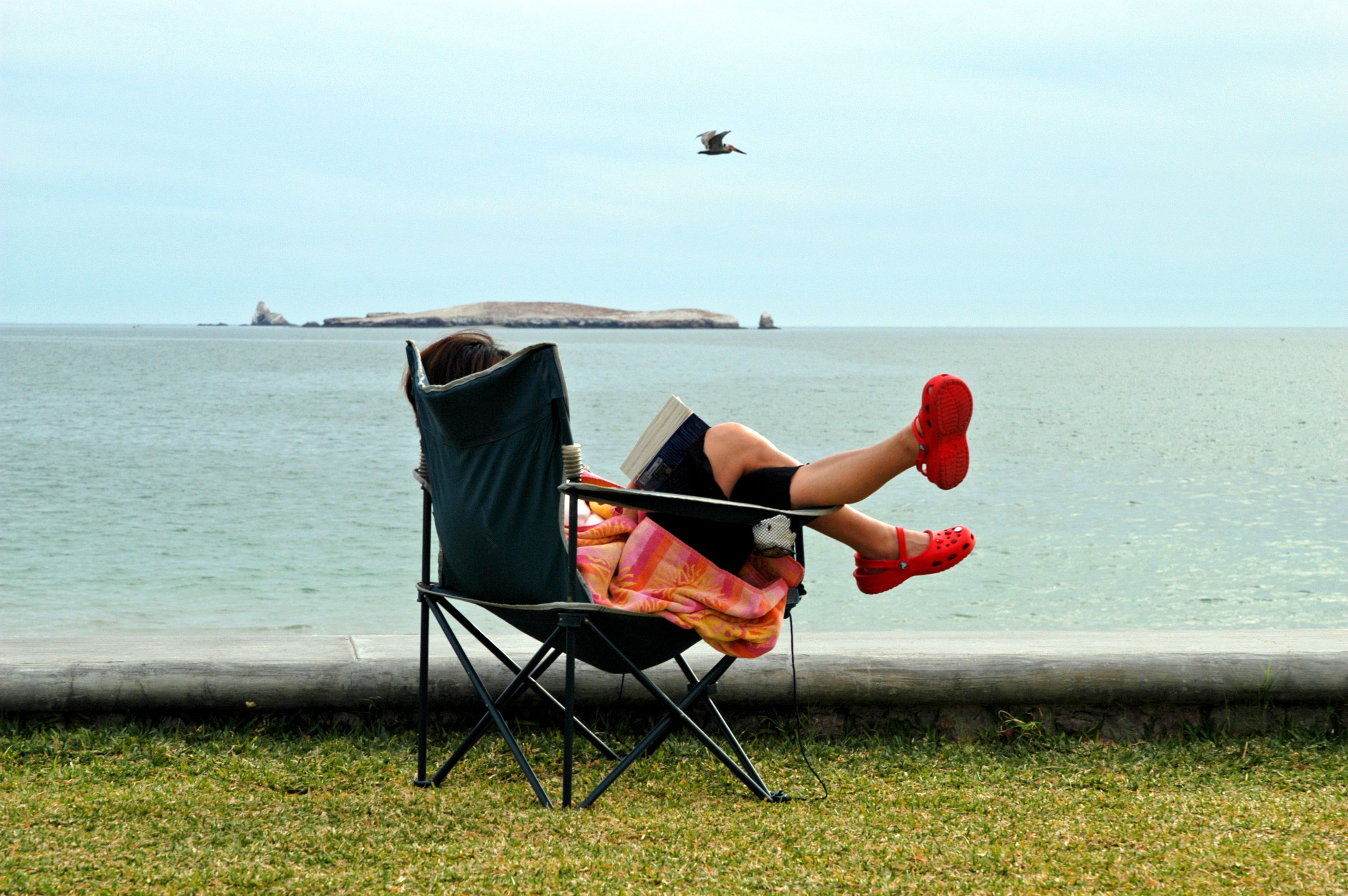 A person sitting in a camp chair by the beach with crocs on 