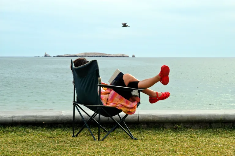 A person sitting in a camp chair by the beach with crocs on