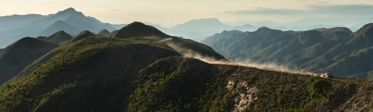 panoramic shot of a 4x4 travelling along a mountain trail, kicking up dust