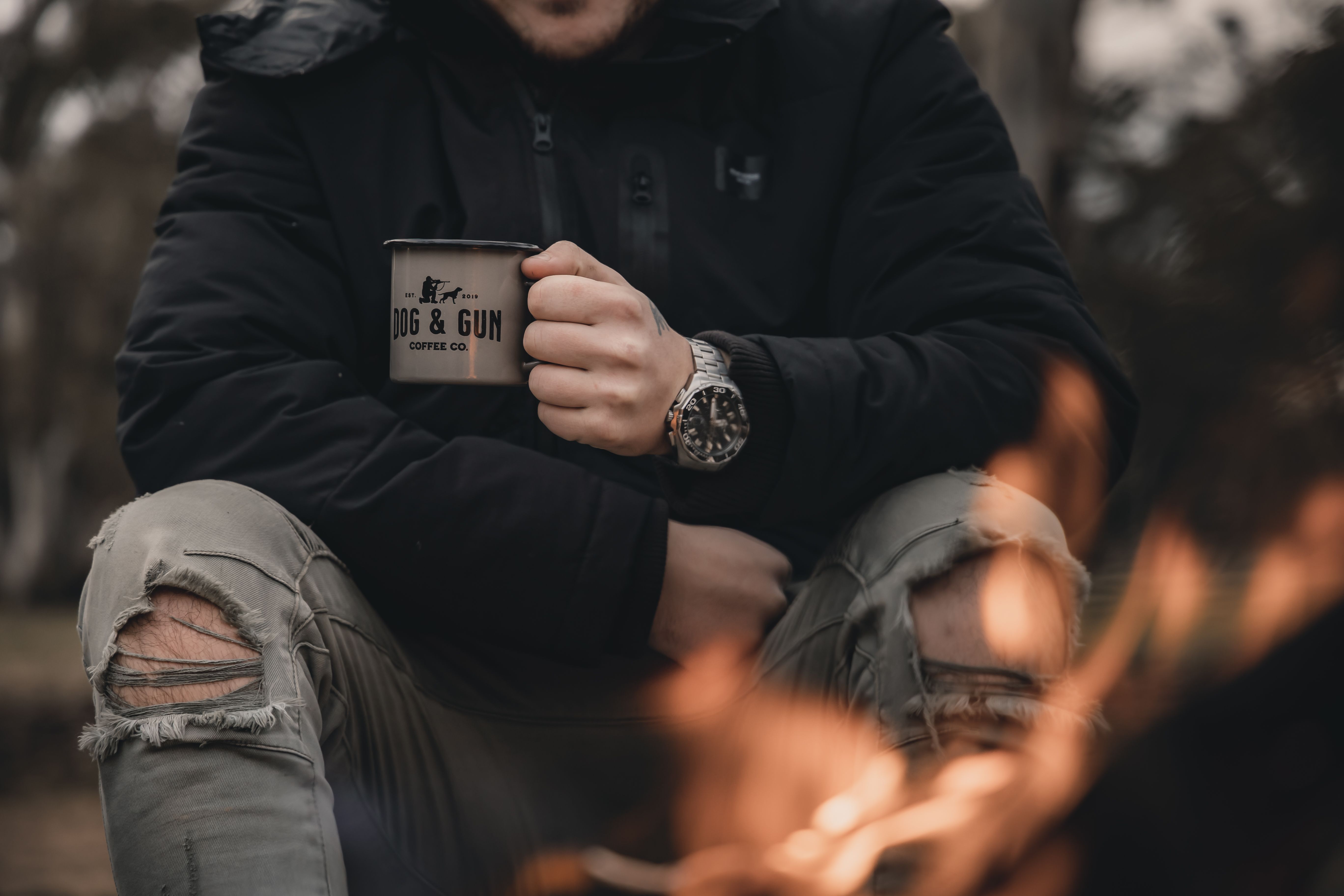 A man by a campfire, nursing a mug of coffee