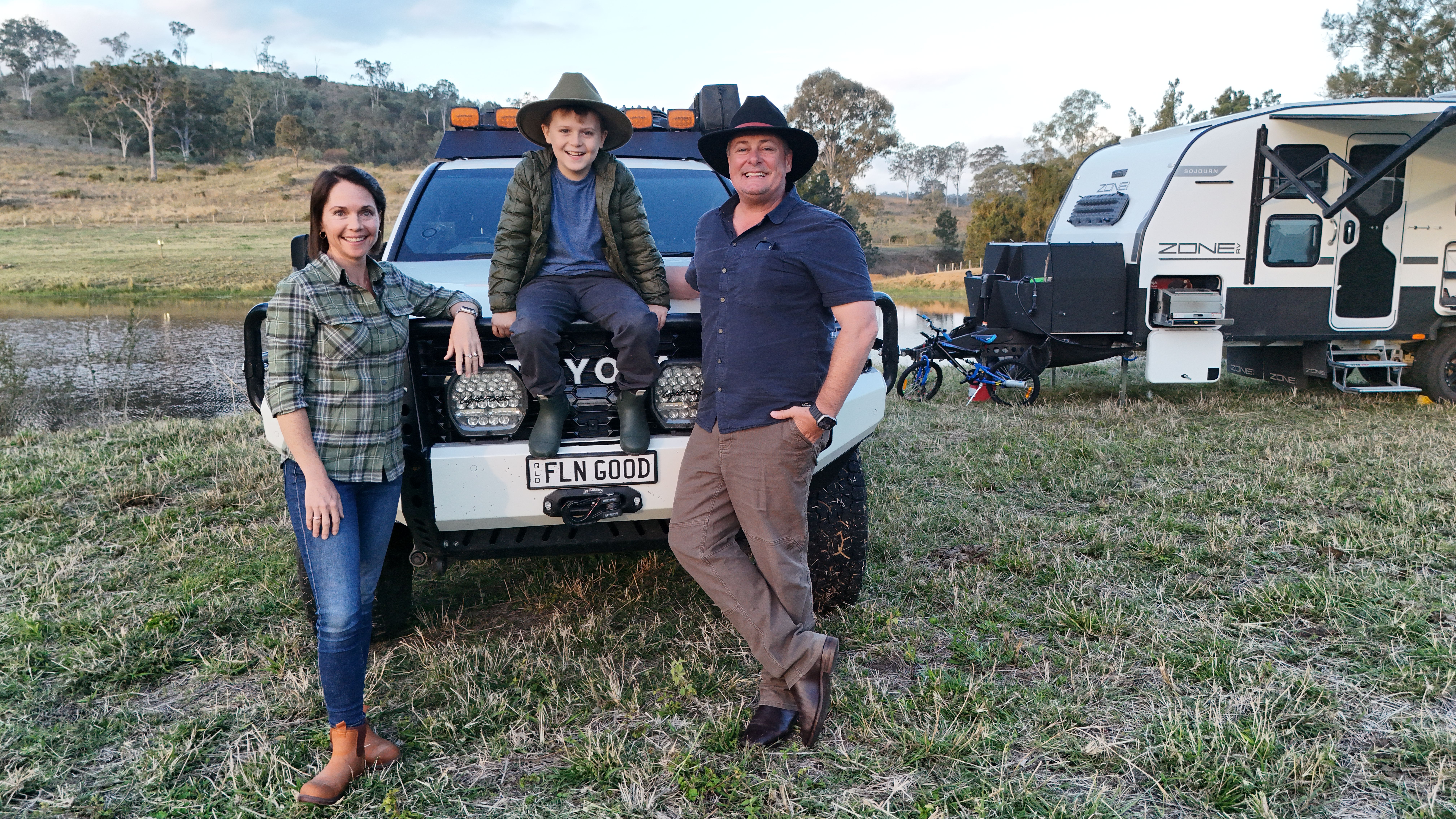 FAMILY SITTING ON A 4WD WITH A CARAVAN IN THE BACKGROUND 