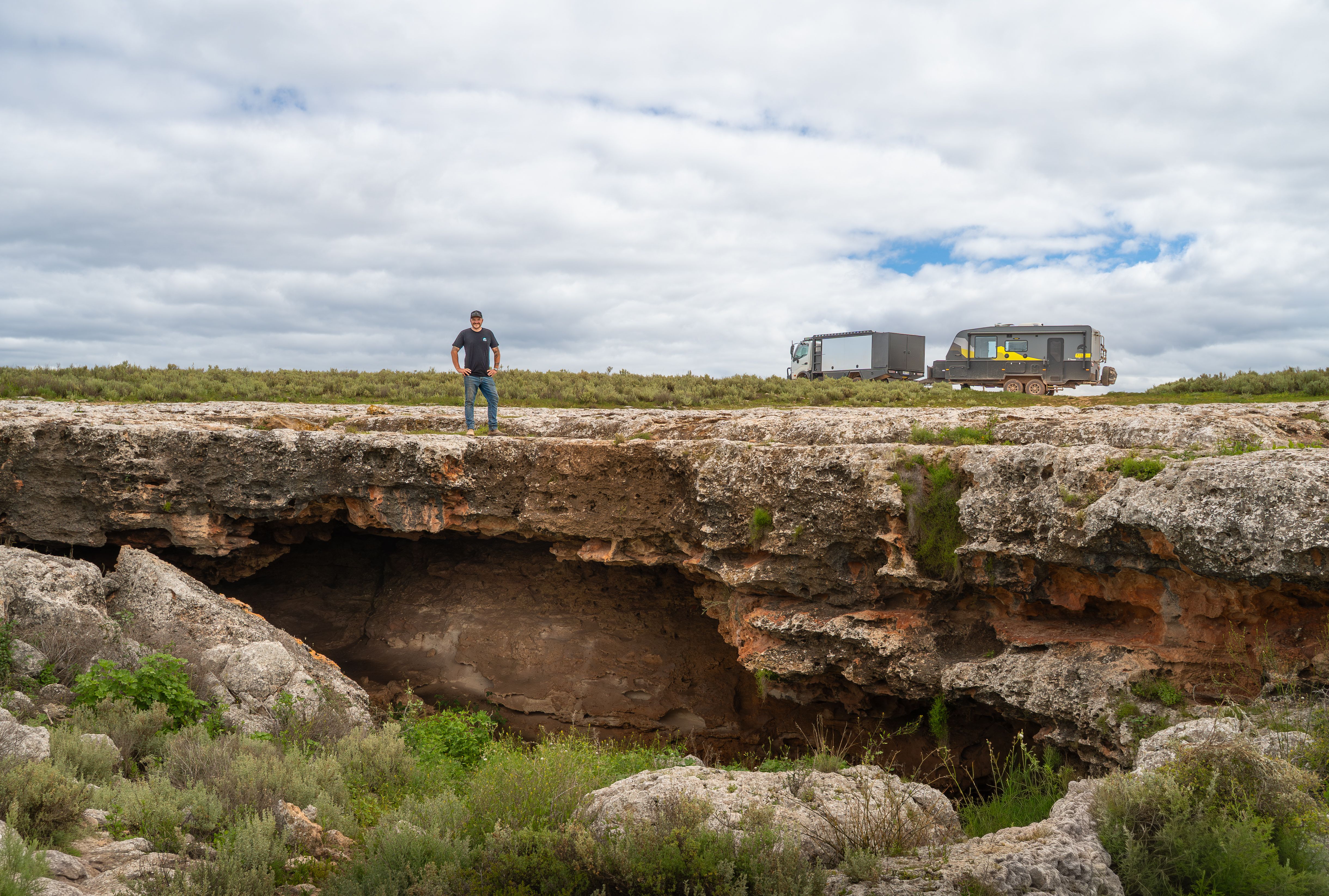 Man standing over a sinkhole with a 4X4 and caravan in the background