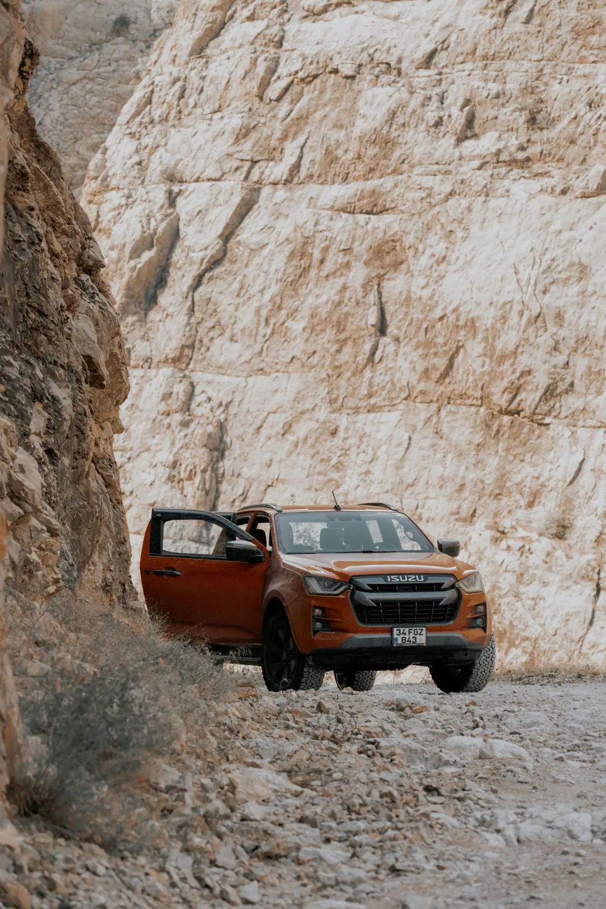 orange 4x4 with open door in front of rock cliff face in desert