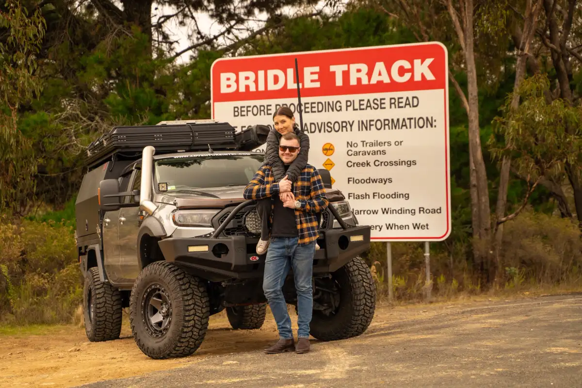 A COUPLE WITH THEIR 4X4 IN FRONT OF A ROAD SIGN