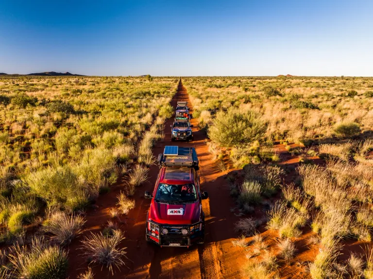 convoy of ford 4x4s driving though desert with small grasses