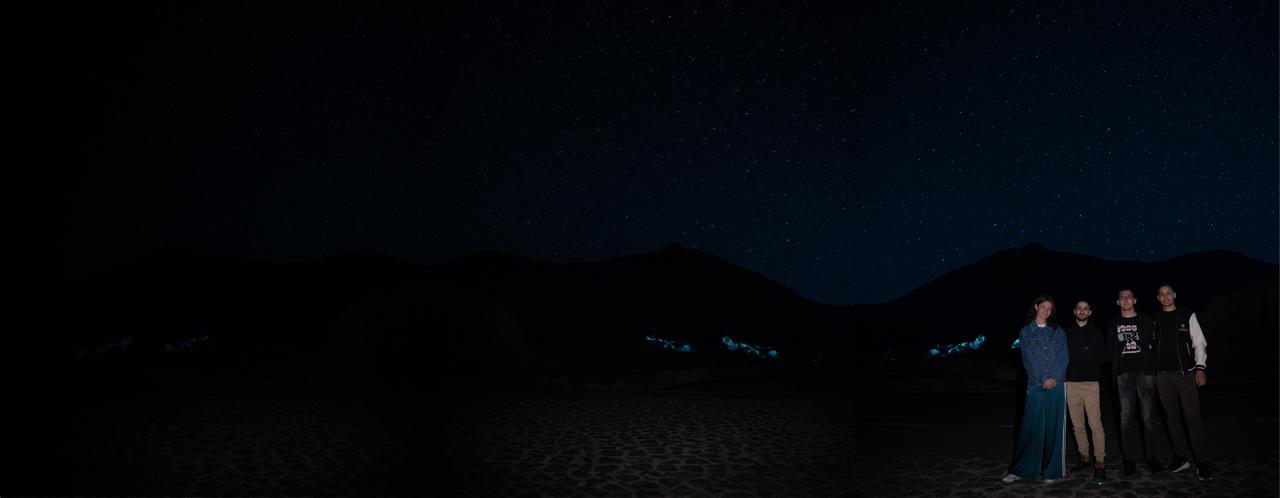 A small group standing together under a starry night sky, mountains behind them