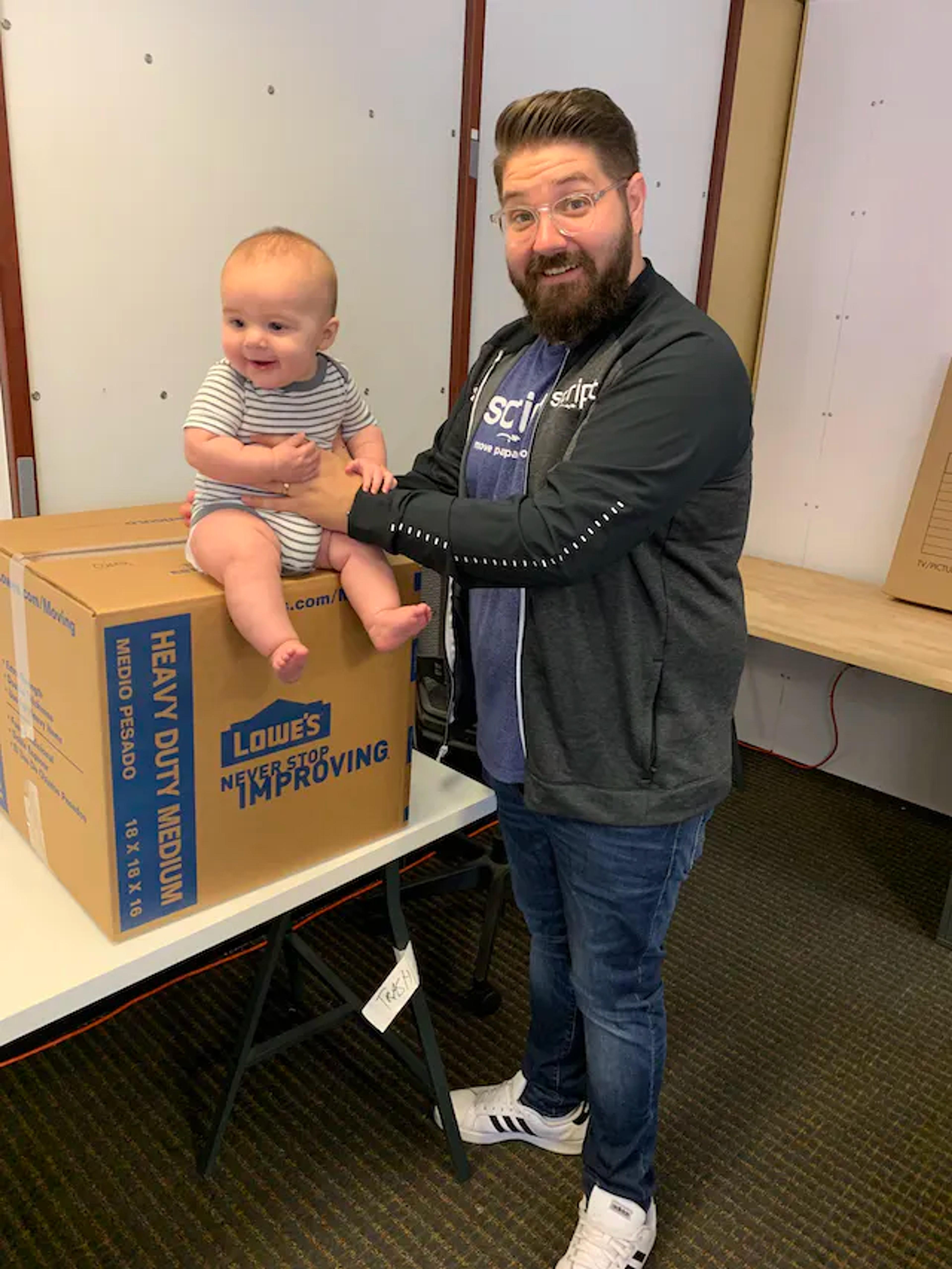 Pat Cahill standing in his office with his son as a baby and some moving boxes at around 270 pounds