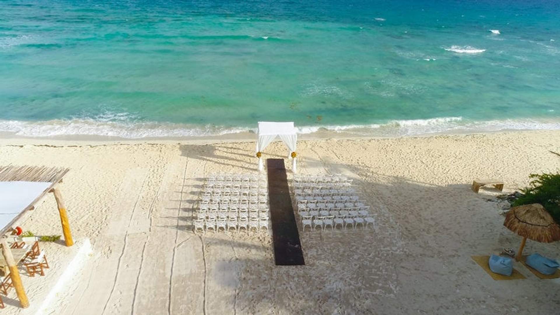 Montaje de recepción de boda en la playa prístina de Punta Venado en Cancún, con un impresionante fondo de océano y elegantes sillas blancas.