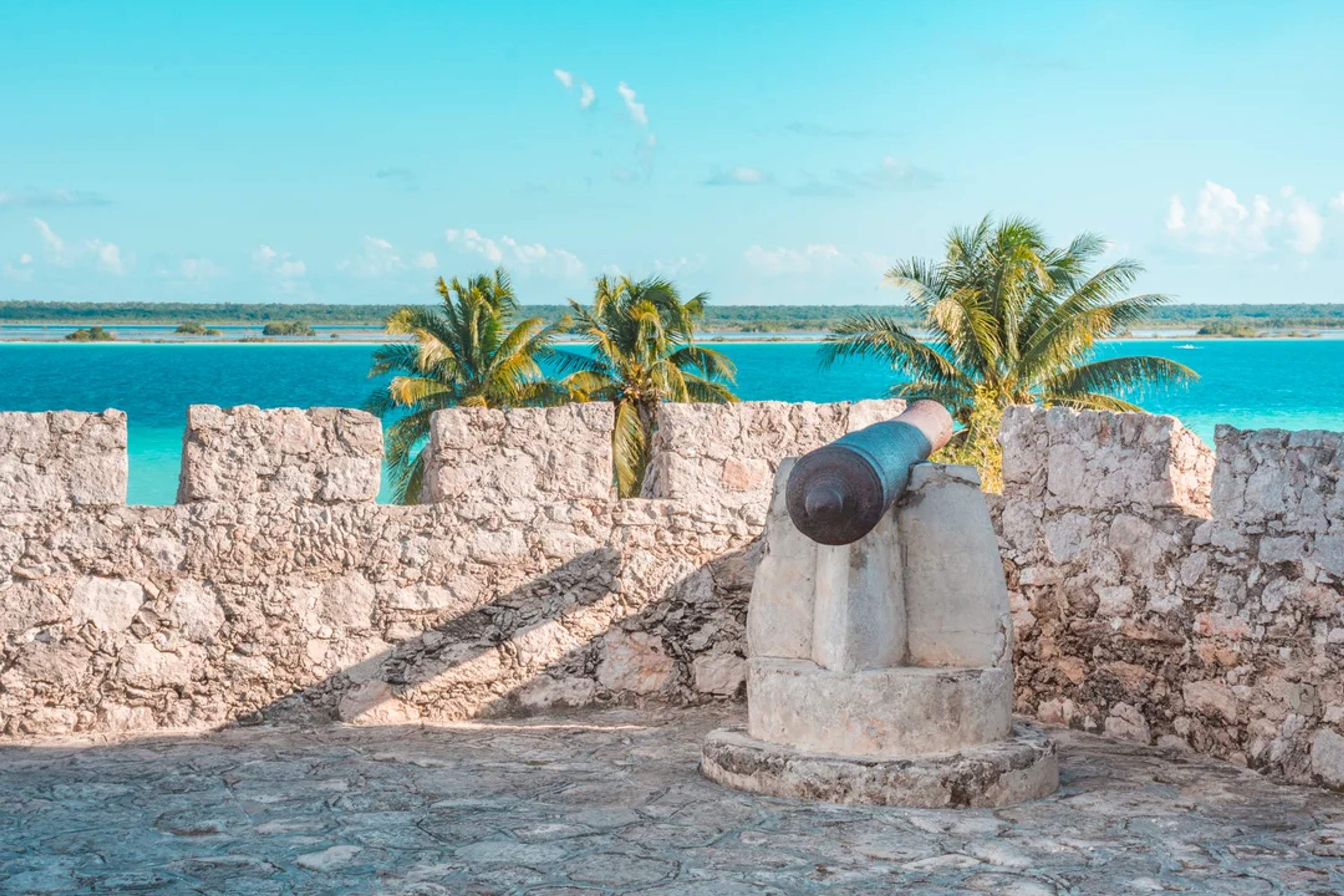 Historic cannon overlooks the turquoise lagoon from a stone fort in Bacalar, Mexico.