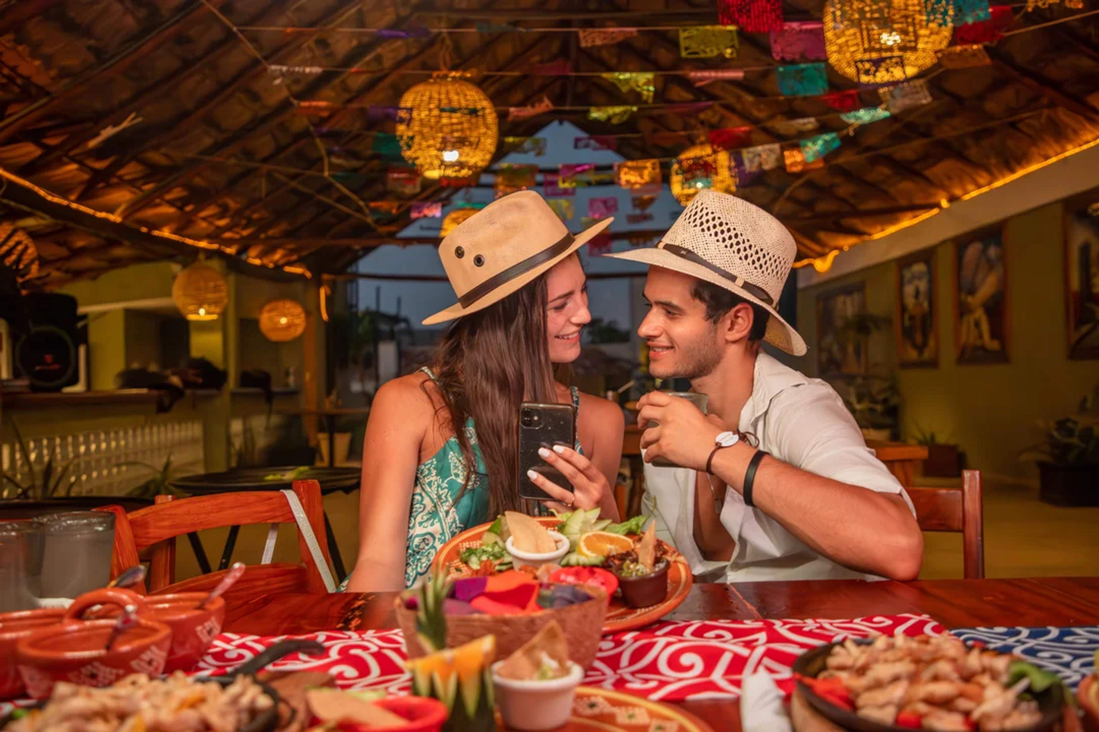 Pareja disfrutando una cena romántica mexicana bajo luces cálidas y coloridos papeles picados.