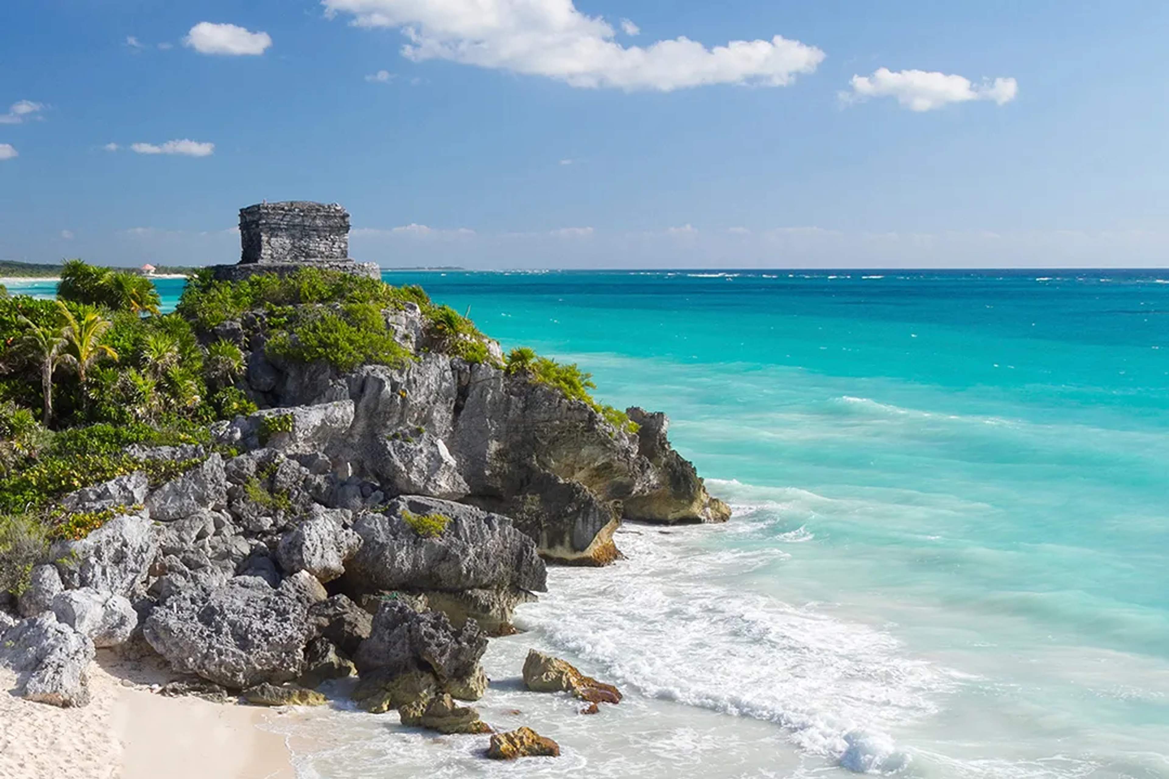 Tulum ruins perched on a cliff, overlooking the turquoise Caribbean Sea and white sandy beach.