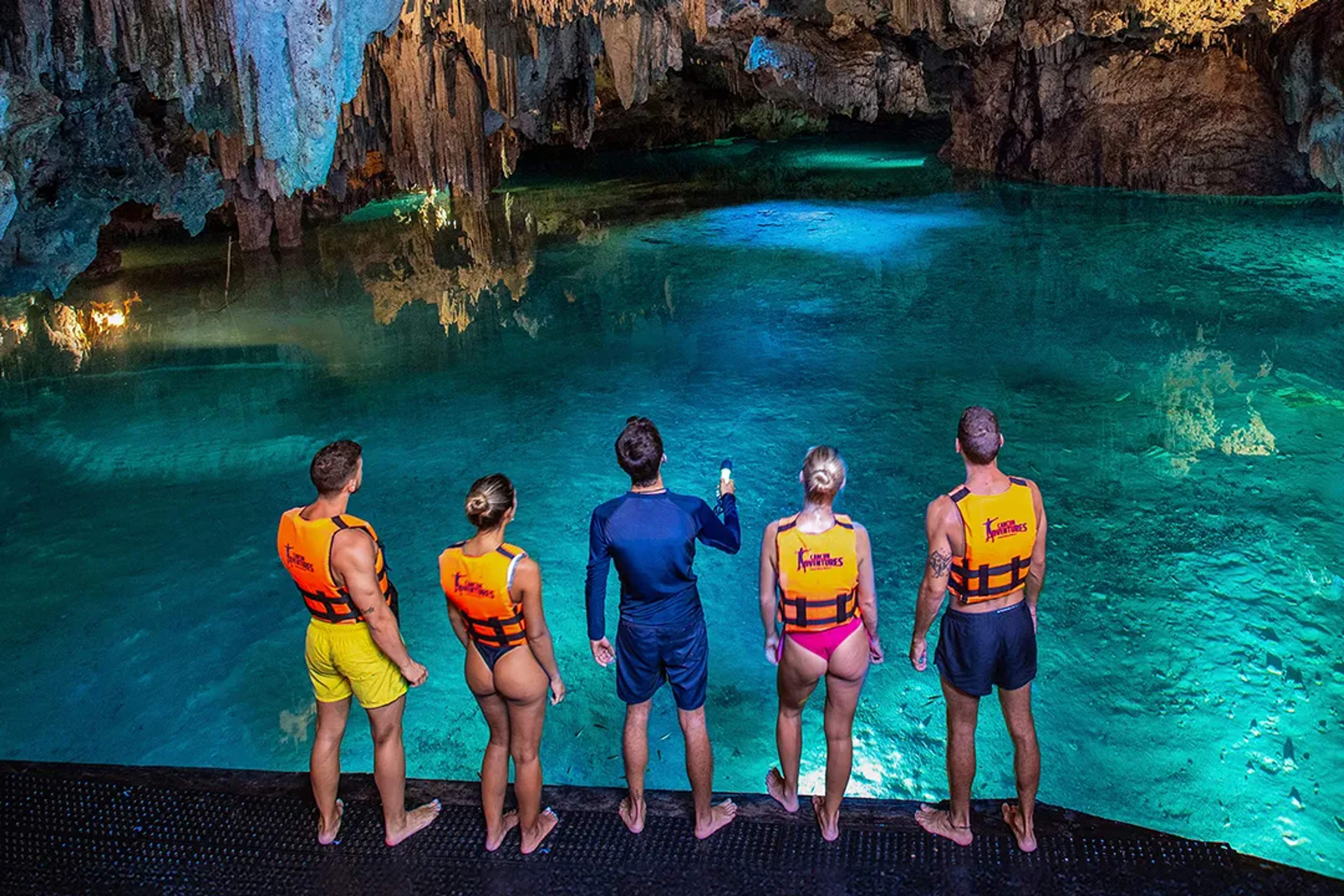 Visitors preparing to swim in underground cenote cave with crystal-clear water and stalactite formations tour