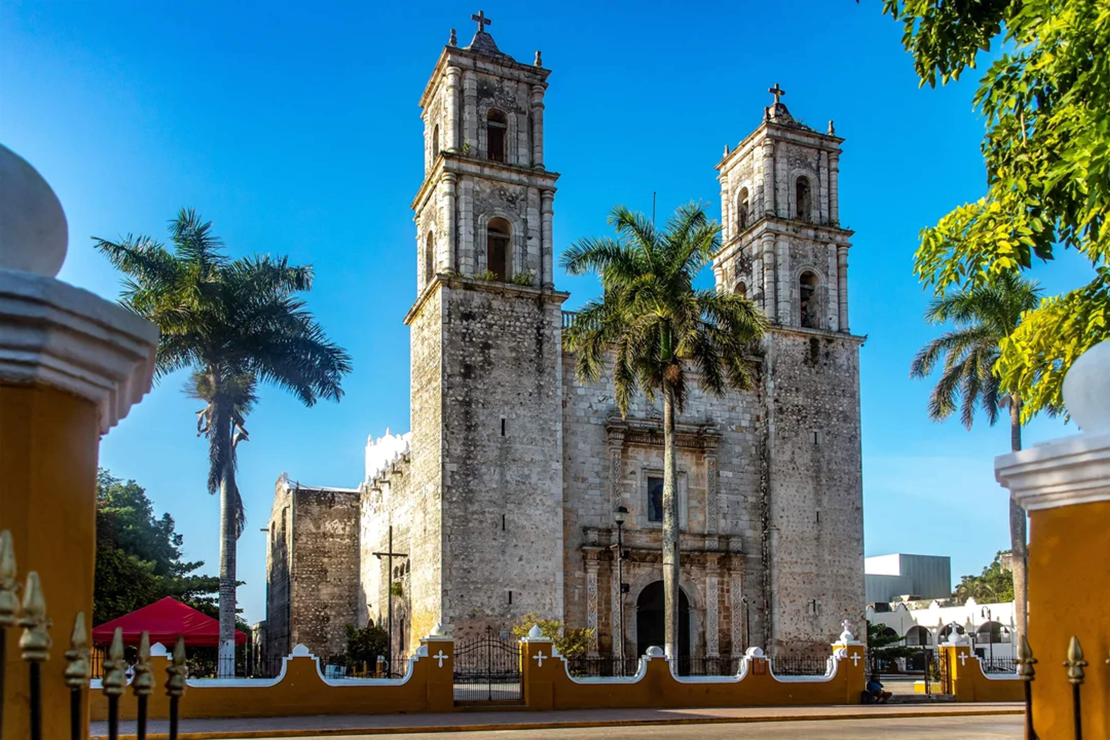 Majestic colonial church with two towers and palm trees in front, under a clear blue sky on a sunny day in Valladolid.